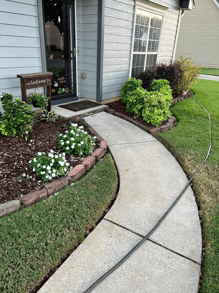 Freshly cleaned curved concrete walkway with pressure washing hose visible